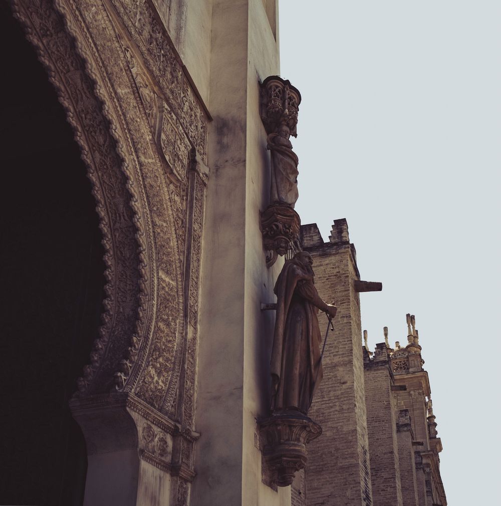Gothic stone statues and intricate carved archway detail on Seville Cathedral exterior wall.