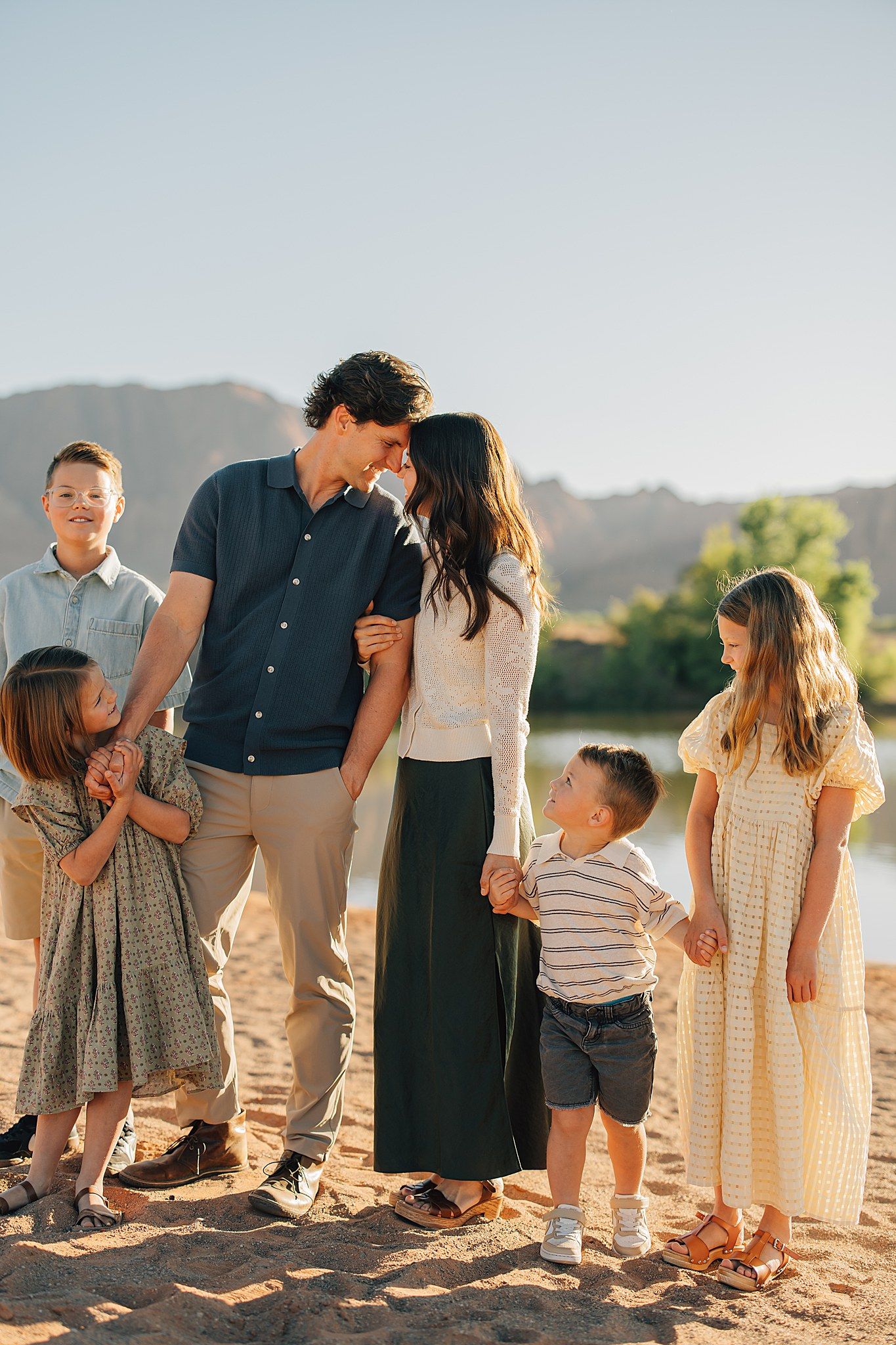 Family of six sharing a tender moment on a sandy beach with mountain backdrop in warm golden light.