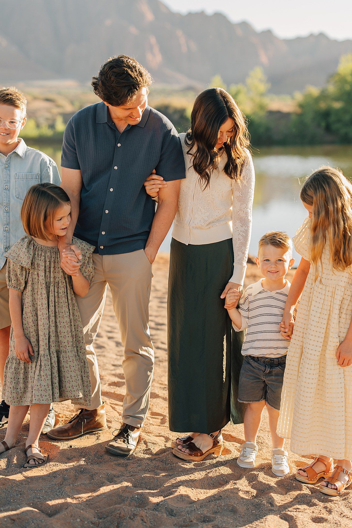 A happy family of six poses outdoors near a river with red rock formations in warm golden light.