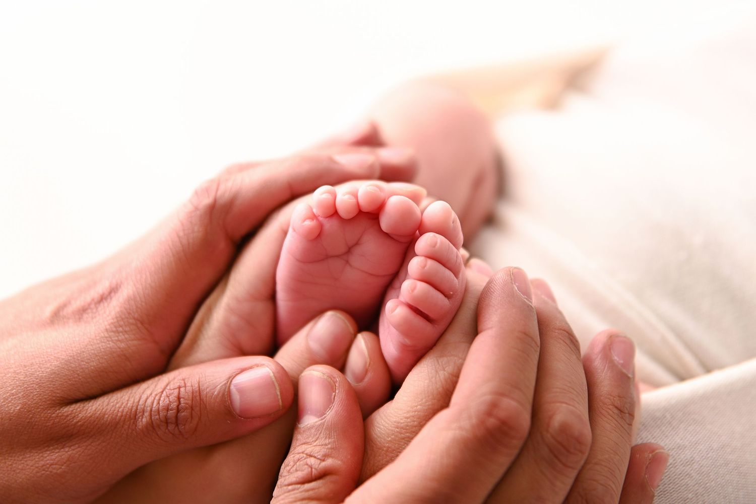 Adult hands gently cradling tiny newborn baby feet in a tender, loving close-up moment.