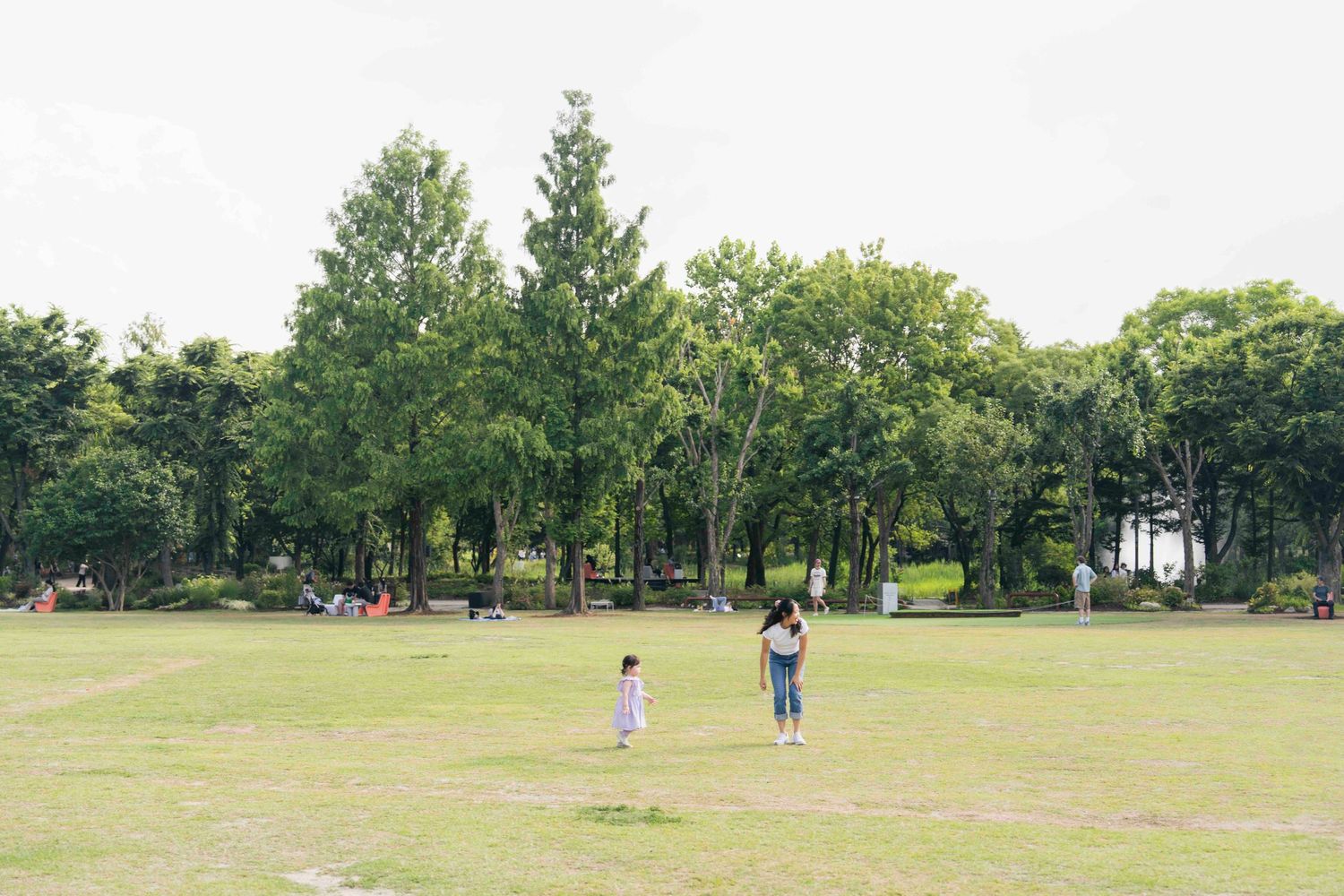 Two children playing in a lush green park surrounded by tall trees on a cloudy day.