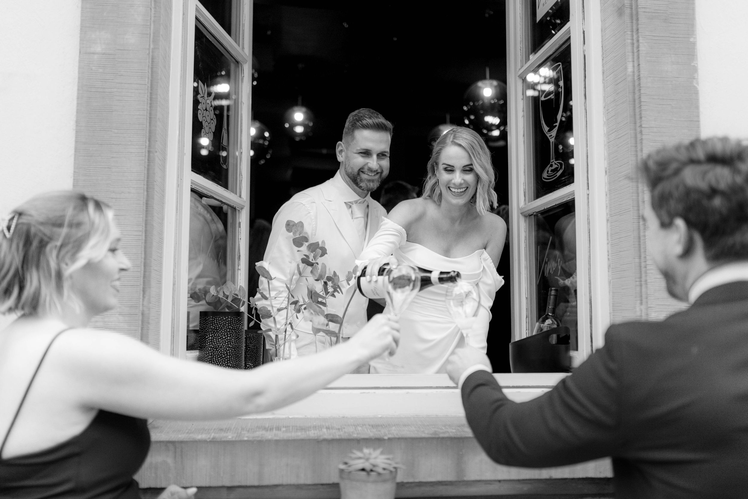 Wedding guests raise their glasses in celebration during an elegant indoor reception at a white-walled venue.