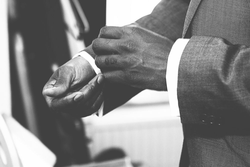 Black and white photo of a man in a suit adjusting his cufflinks, showcasing elegant formal attire. At Oaks farm wedding venue in Surrey