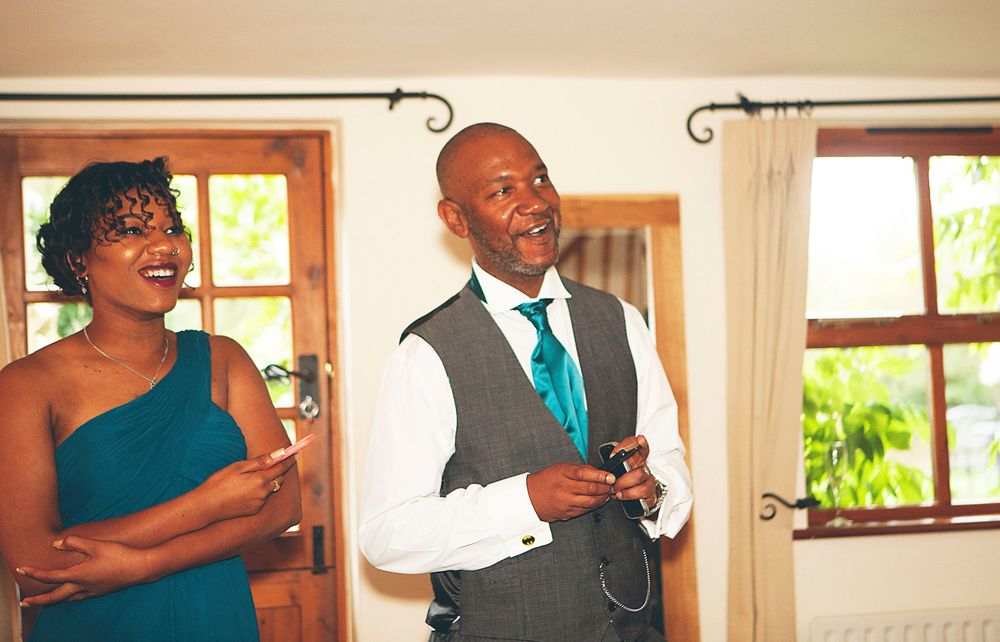 A man and woman smile during a wedding speech, man wearing a vest and teal tie, woman in a teal dress. At Oaks farm wedding venue in Surrey