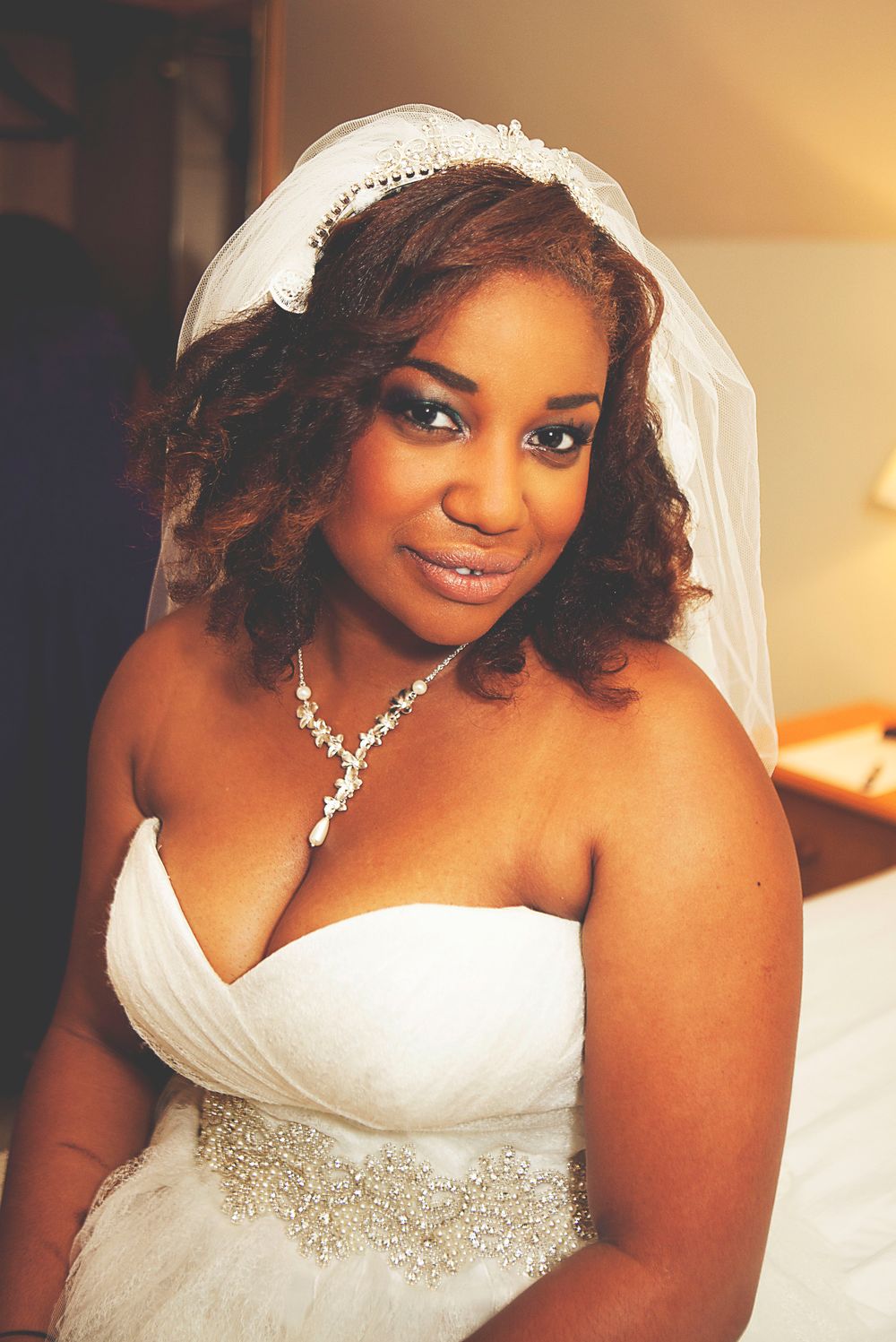 A beautiful bride in a white strapless gown with a veil and diamond necklace smiles warmly on her wedding day. At Oaks farm wedding venue.