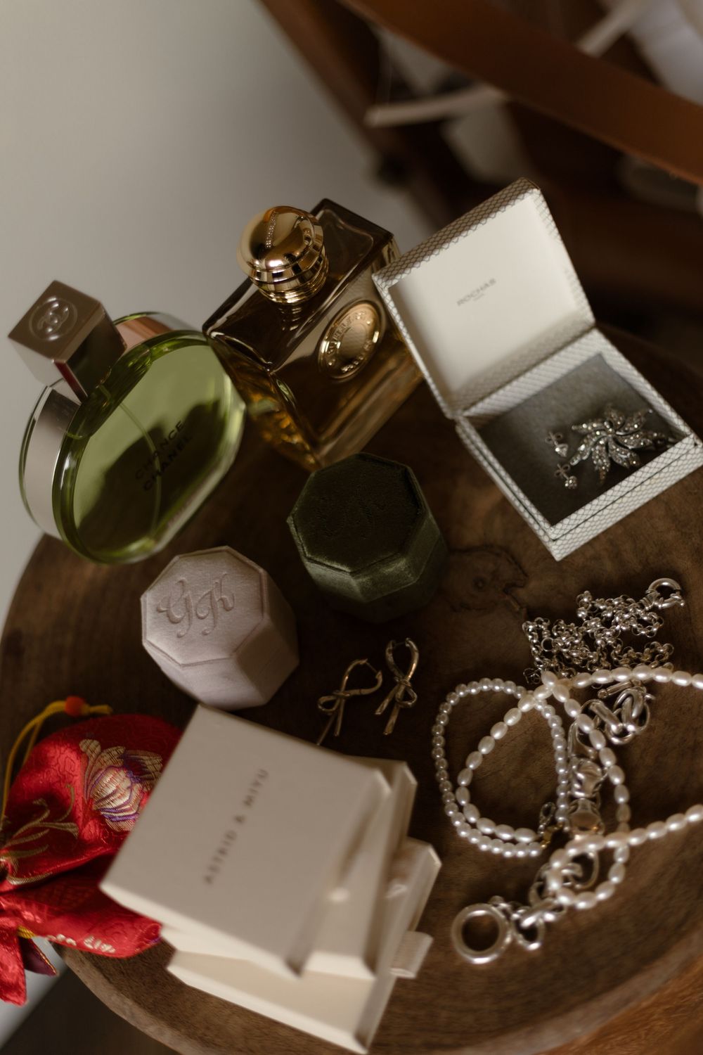 Elegant flat lay of perfume bottles, jewelry boxes, pearl necklace, and accessories arranged on a wooden table.