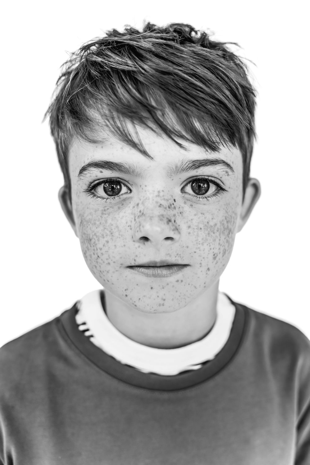 Black and white close-up portrait of a freckled boy with short hair wearing a gray shirt.