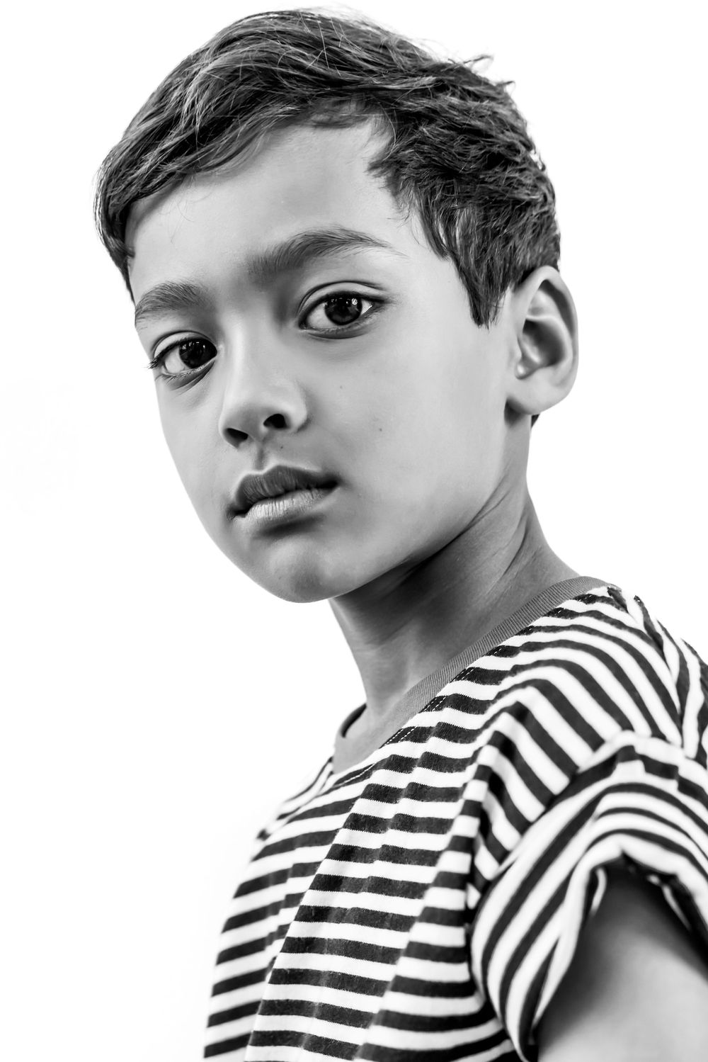Black and white portrait of a young boy in a striped shirt looking at the camera.