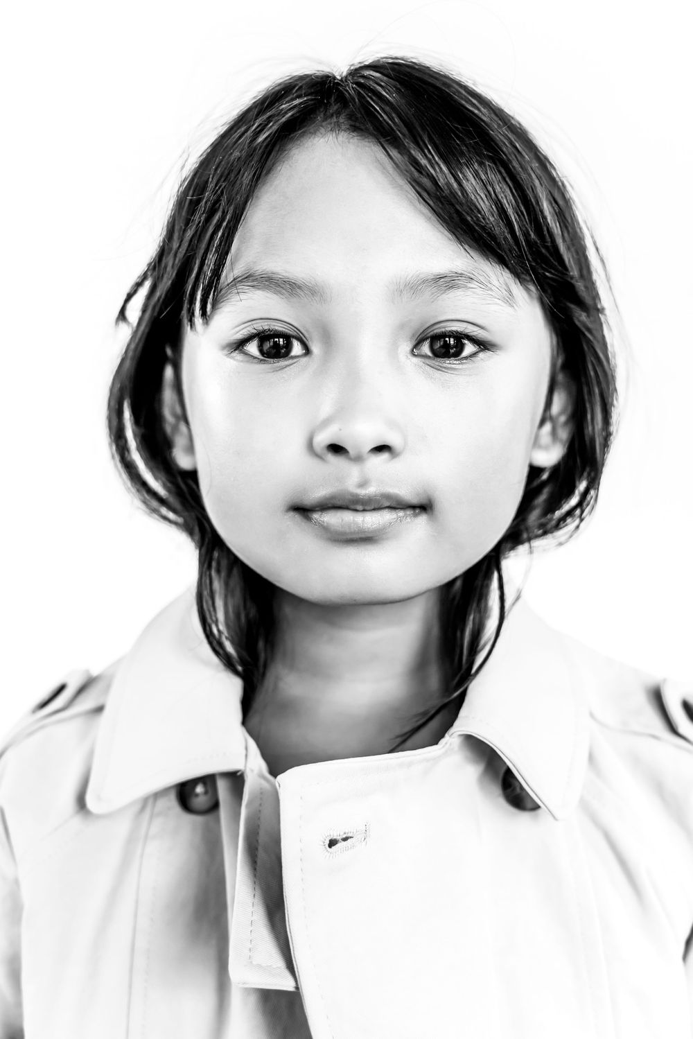 Black and white portrait of a young Asian girl with dark hair wearing a light jacket, looking directly at camera.
