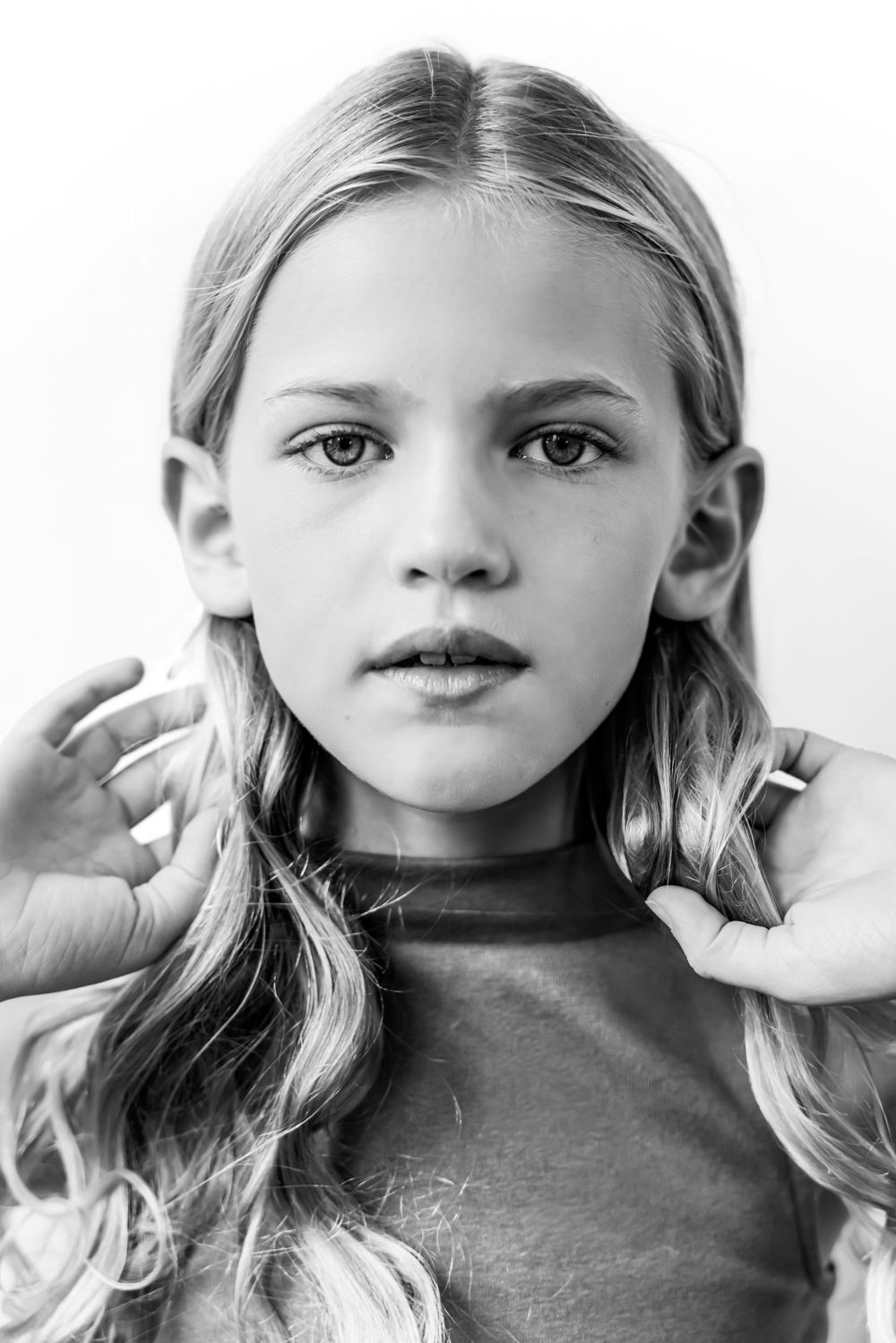 Black and white portrait of a young girl with long wavy blonde hair holding her hair back.