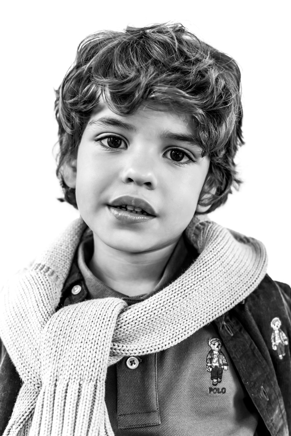 Black and white portrait of a young boy with curly hair wearing a Polo shirt and knit scarf.