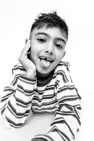 Black and white portrait of a playful boy in a striped shirt sticking his tongue out cheekily.