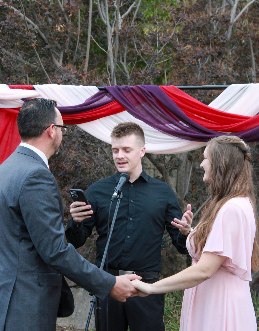 A group of formally dressed people stand in a line outdoors with red and white decorative draping visible behind them.
