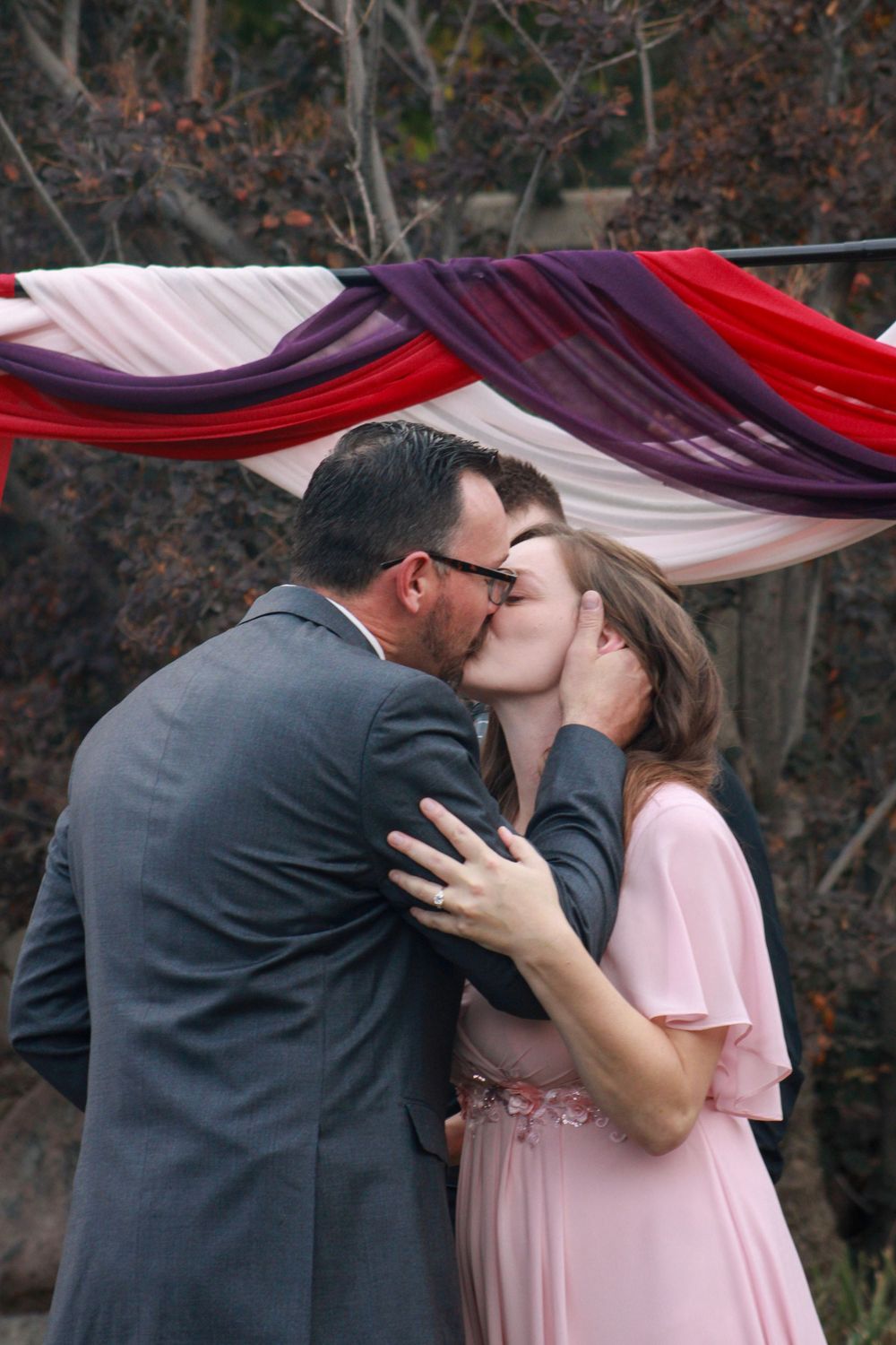 A romantic sequence of photos showing a couple in a pink dress and gray suit embracing under red and purple draping.