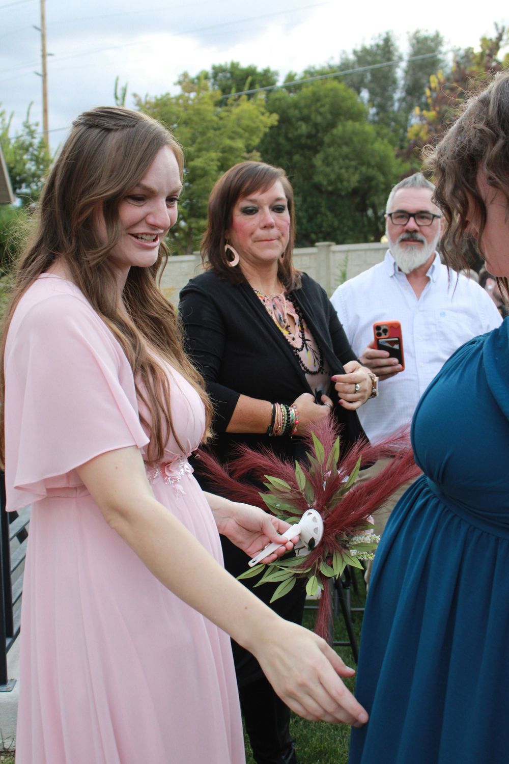 Wedding party members in pink and navy dresses gather outdoors during a celebration.