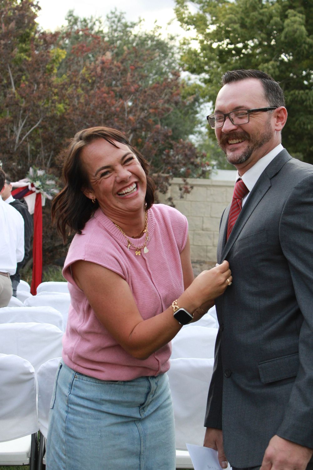 A candid sequence of a couple laughing together outdoors, with the woman wearing pink and the man in a grey suit.