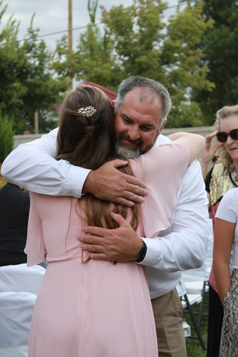 A heartfelt embrace between people wearing pink and white at an outdoor gathering.
