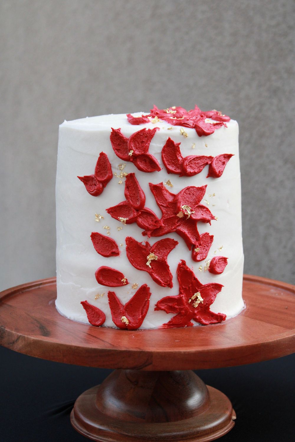White wedding cake decorated with cascading red sugar flowers displayed on a wooden cake stand.