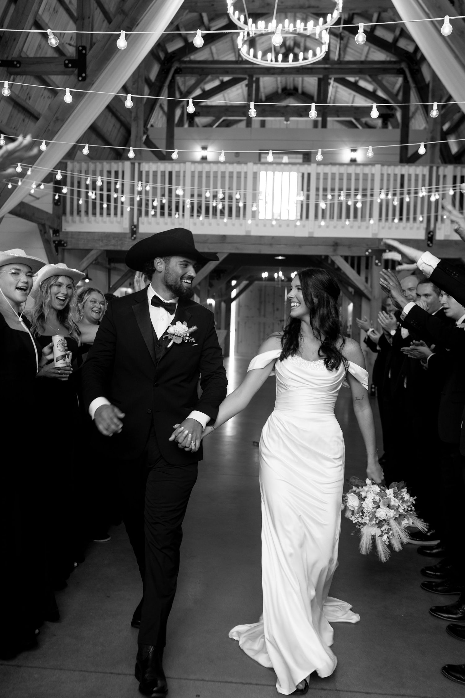 Black and white photo of bride and guests dancing with glow sticks at a rustic barn wedding reception.