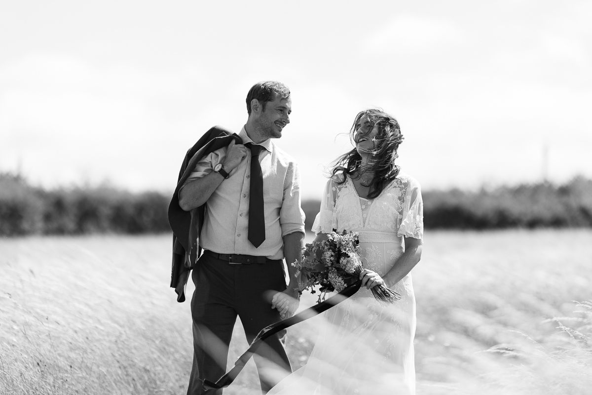 Black and white photo of a bride and groom laughing together in a field on their wedding day.