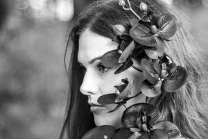 Black and white portrait of a young woman with long hair adorned with large black orchids.