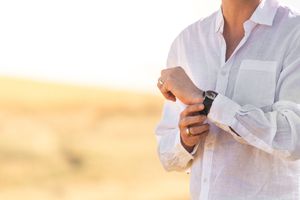 Man in white linen shirt adjusting his black watch outdoors in golden sunlight.