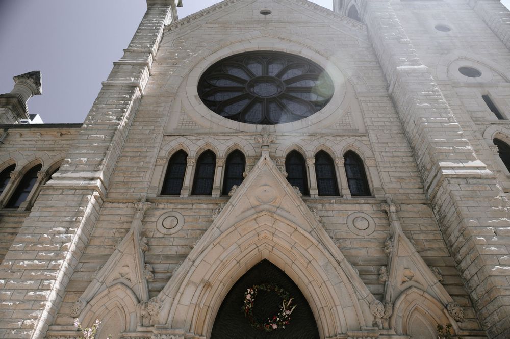 Gothic stone cathedral facade with rose window, arched doorway, and ornate architectural details photographed from below.