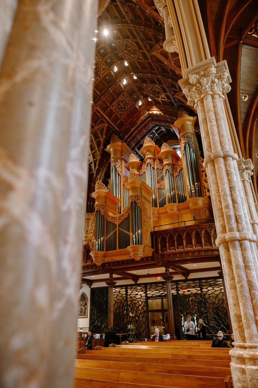 Grand pipe organ with ornate wooden casing inside a Gothic cathedral with vaulted ceilings and stone columns.