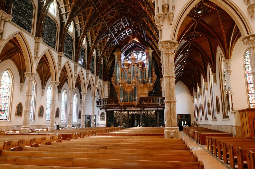 Grand Gothic cathedral interior with wooden pews, soaring arched ceilings, stained glass windows, and a large pipe organ.