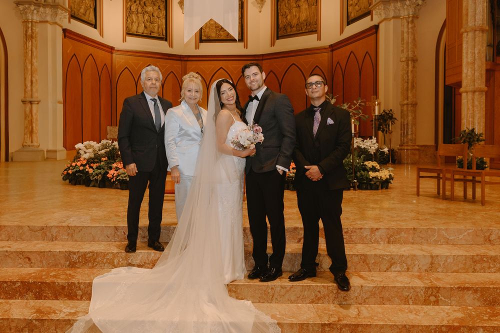 Bride and groom pose with family members inside an elegant church with floral arrangements.