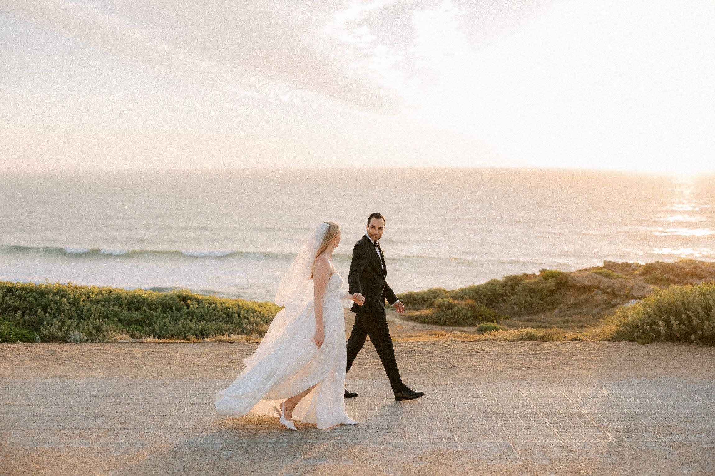 Newlyweds walking together along the Atlantic coastline after their wedding ceremony at Arriba by the Sea in Cascais. Elegant destination we