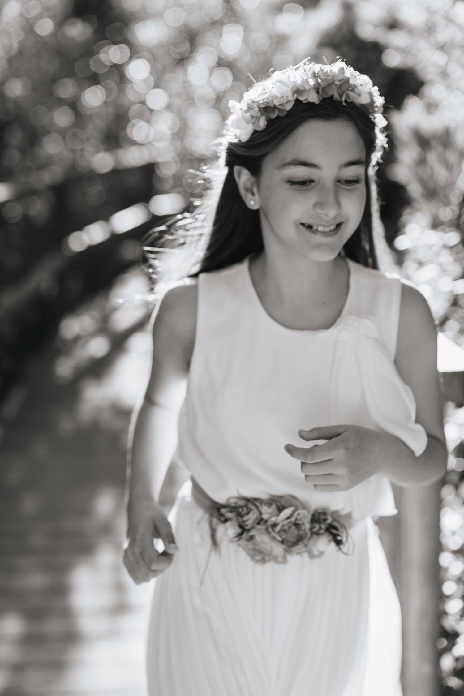 Black and white photo of a smiling girl in white dress and floral crown running outdoors.