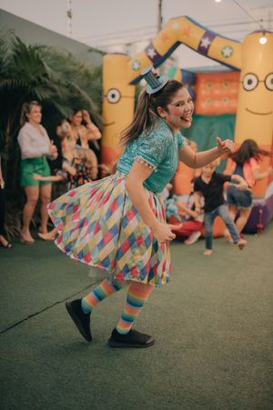 A person dancing in a colorful geometric skirt and turquoise shirt at a themed party.