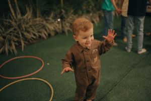 A small child in brown overalls playing on artificial grass at a party.
