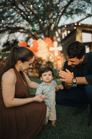 A family shares a tender moment on the grass at sunset with string lights and trees in the background.