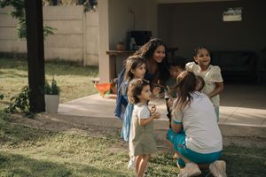 A group of people gather outdoors in a casual setting, enjoying time together in a sunny backyard.