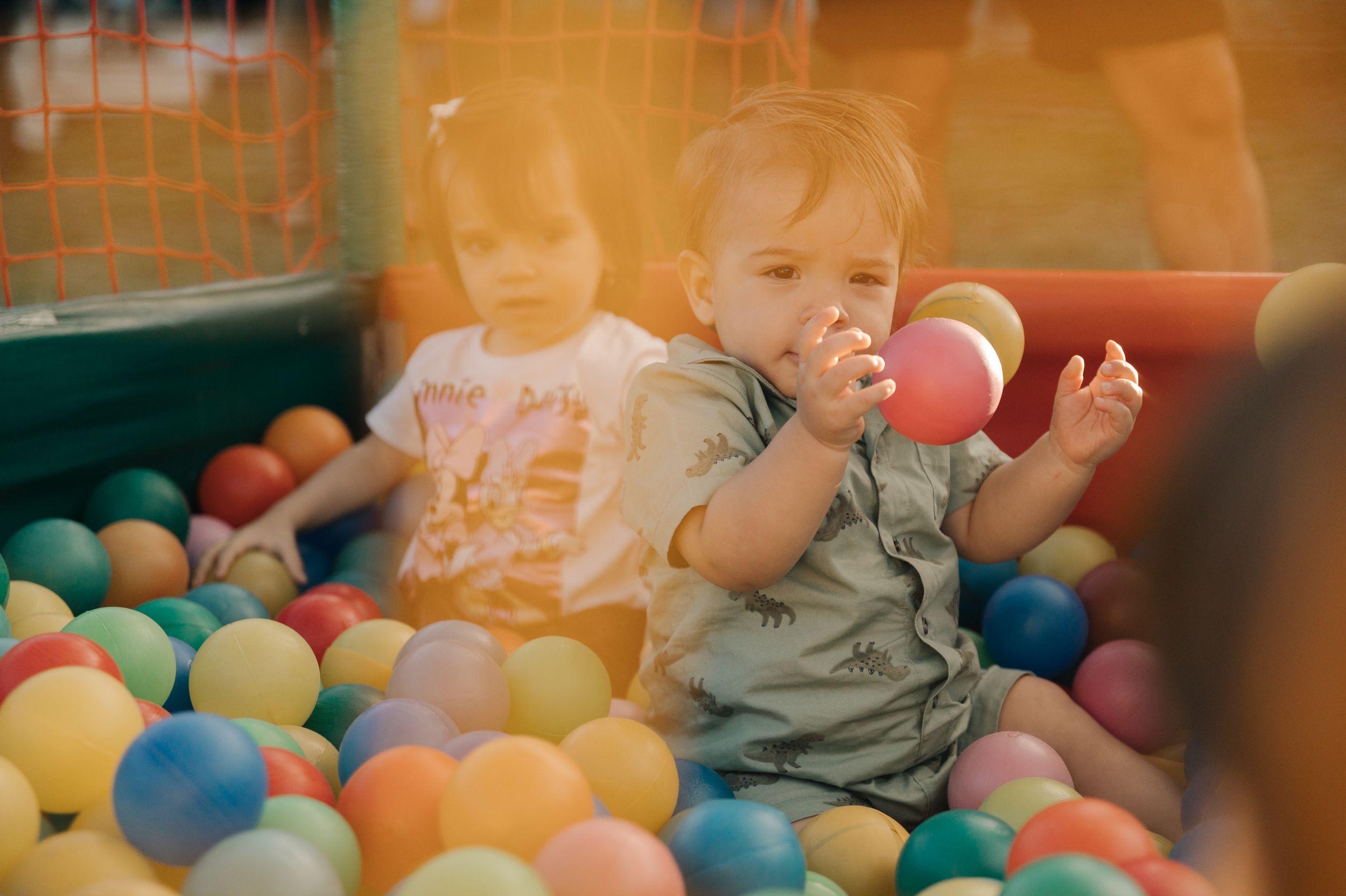 A toddler plays in a colorful ball pit filled with orange, blue, yellow and red plastic balls.