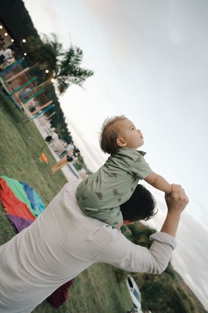 A small child is lifted high into the air at an outdoor event with playground equipment visible in the background.