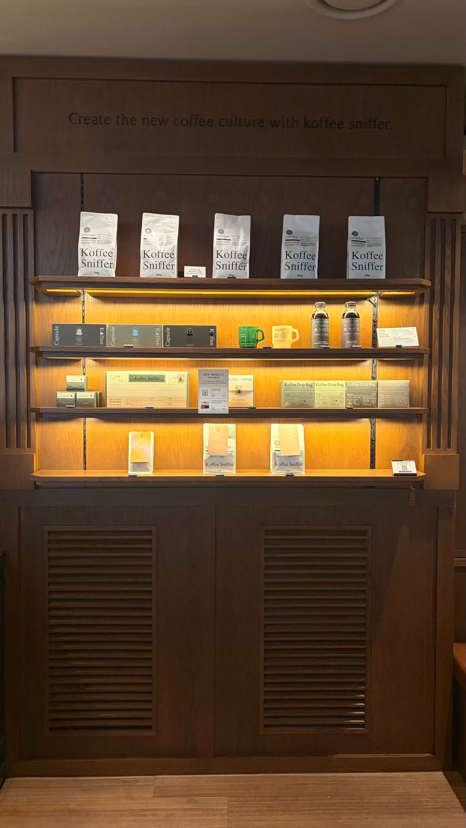 Illuminated wooden display shelf showcasing Koffee Sniffer coffee products and accessories in a modern cafe retail setting.