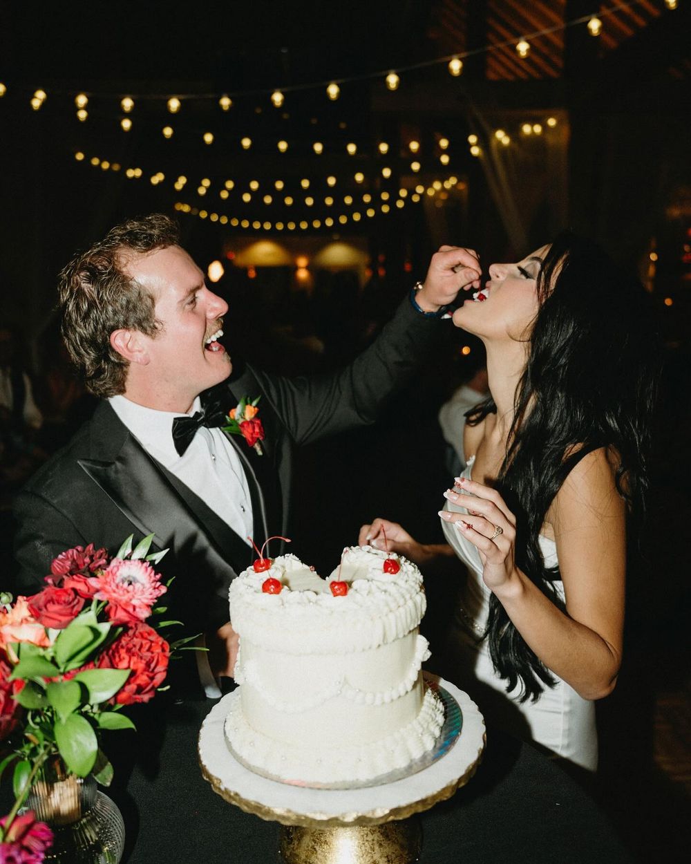 Sarah and Lee cutting the cake under string lights at Mount Norquay