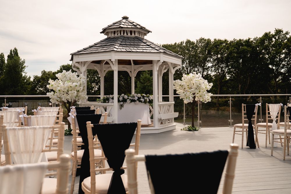 Elegant outdoor wedding ceremony setup with white gazebo, floral arrangements, and gold chiavari chairs on a rooftop terrace.