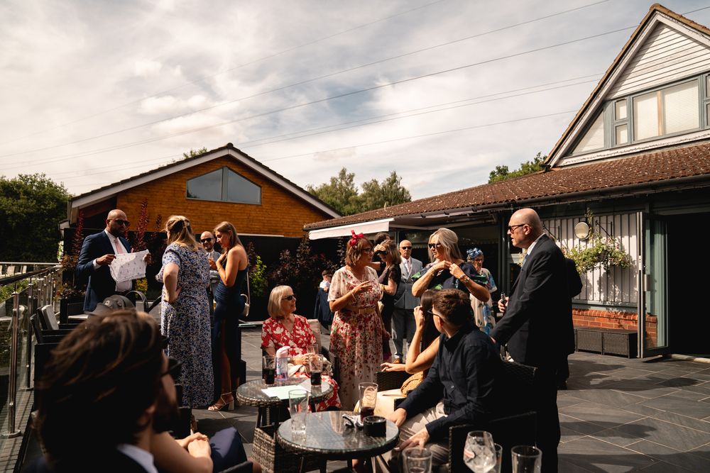 Guests mingle outdoors at a wedding reception on a patio, with buildings and cloudy sky in the background.