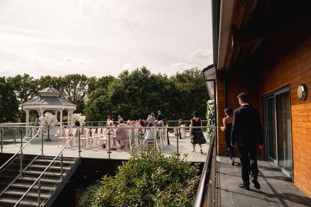 Guests gather on an outdoor terrace with a white gazebo and lush trees at an elegant wedding venue.
