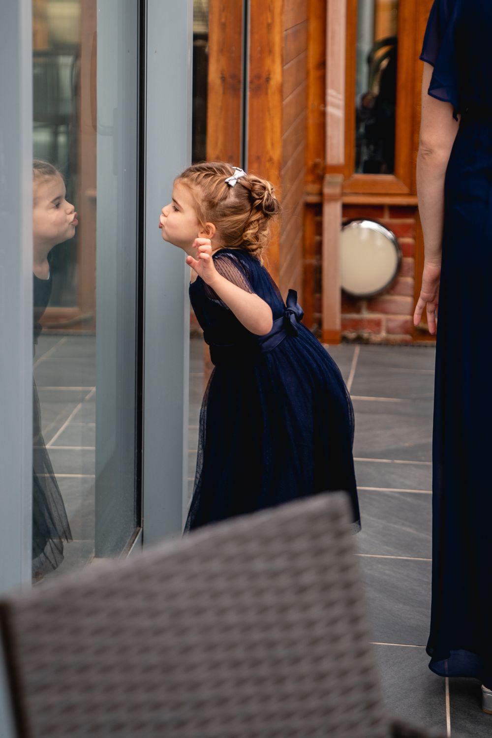 A young girl in a navy blue dress looks through a glass window at a wedding venue.