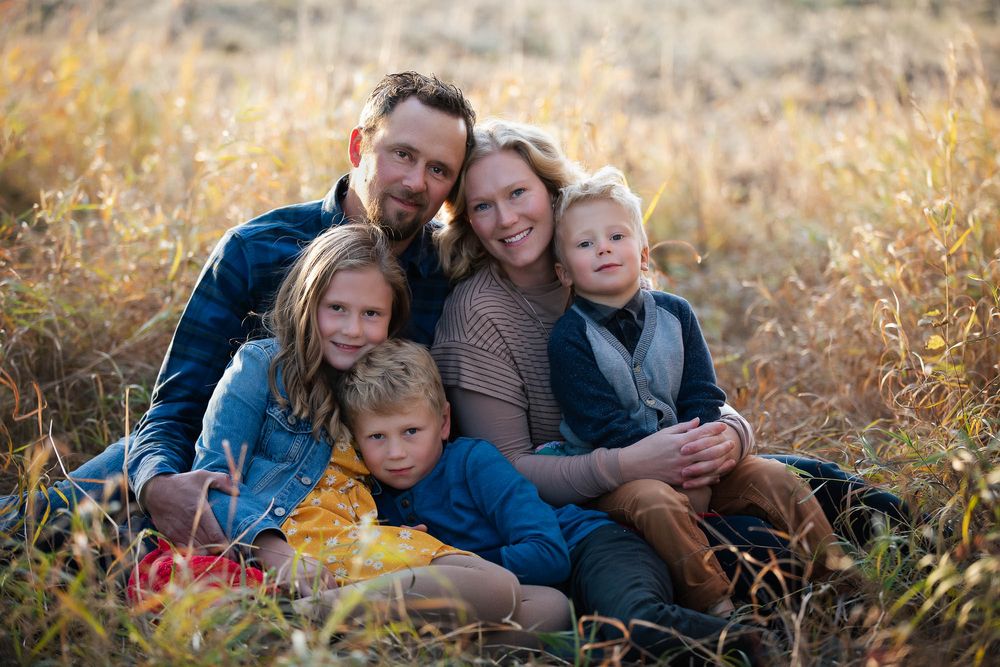 A family sits together in a sunlit field of tall grass during golden hour.