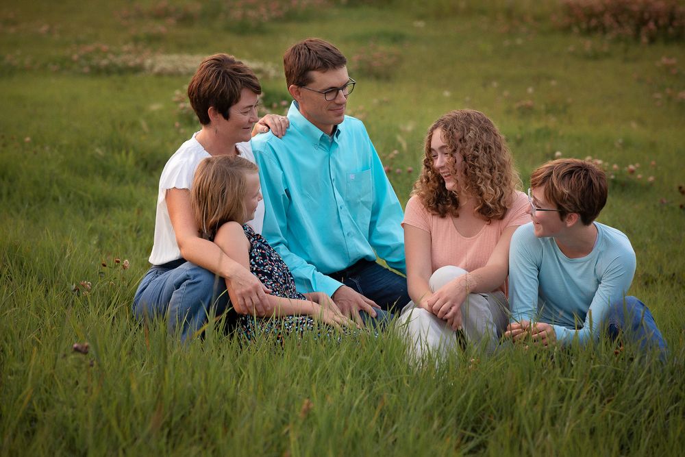 mom, dad and 3 daughters sitting in green grassy field
