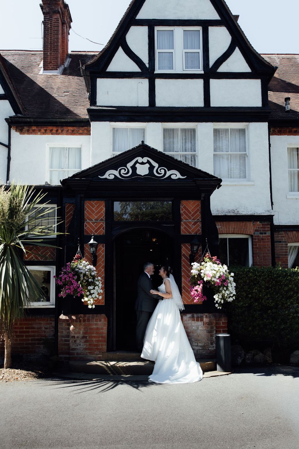 Bride and groom sharing a kiss outside a traditional Tudor-style wedding venue with floral decorations.