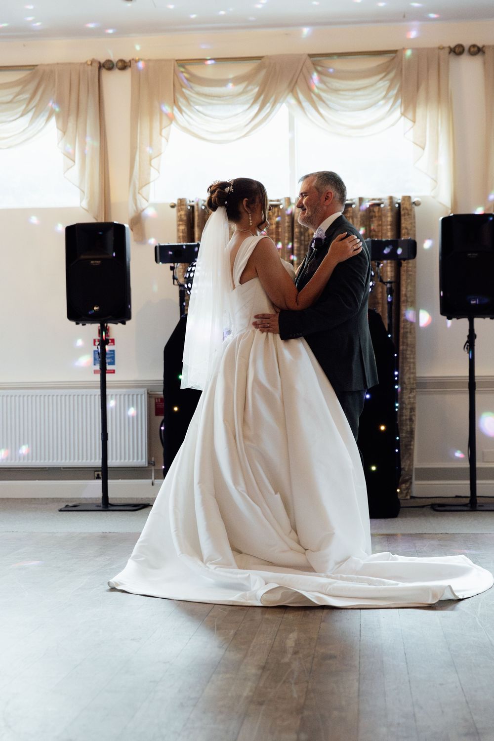 Bride and groom share their first dance in a decorated reception hall, bride wearing a flowing white ball gown.