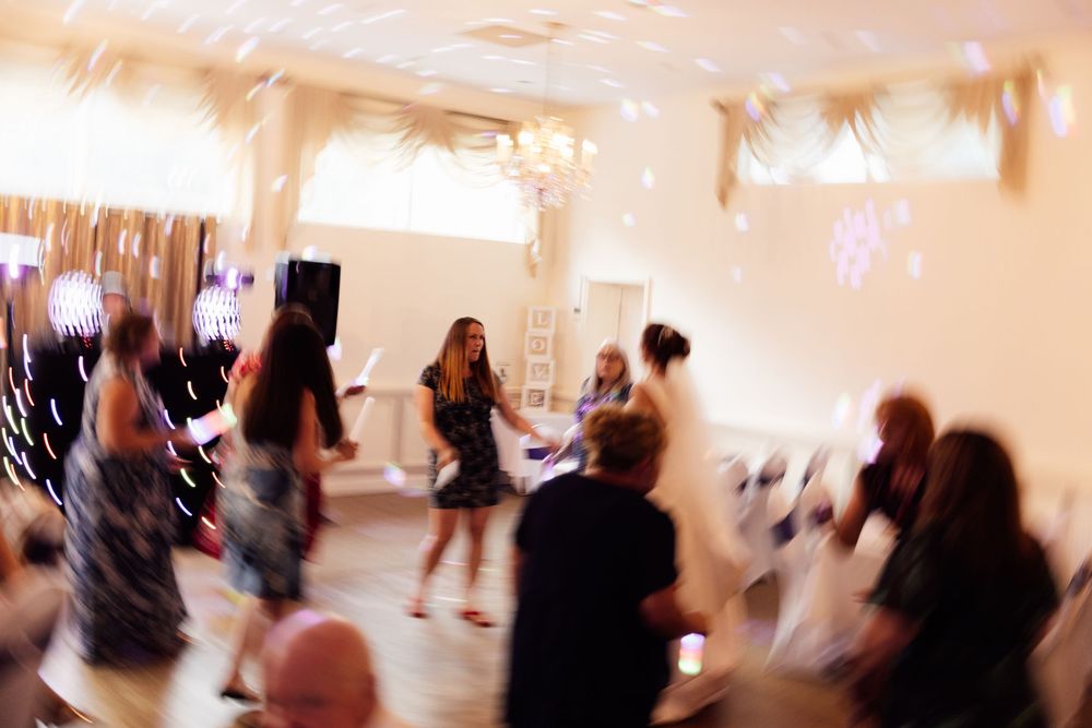 Guests dancing and celebrating at a wedding reception in a decorated ballroom with lights.
