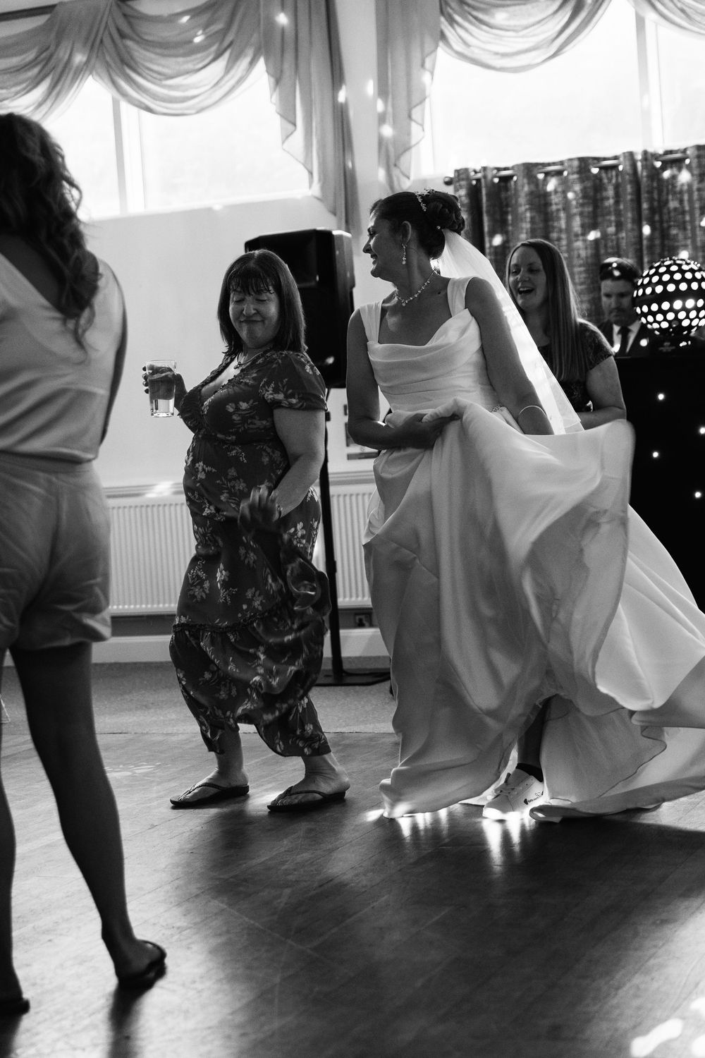 Bride in white gown dancing joyfully with guests at wedding reception in black and white photo.
